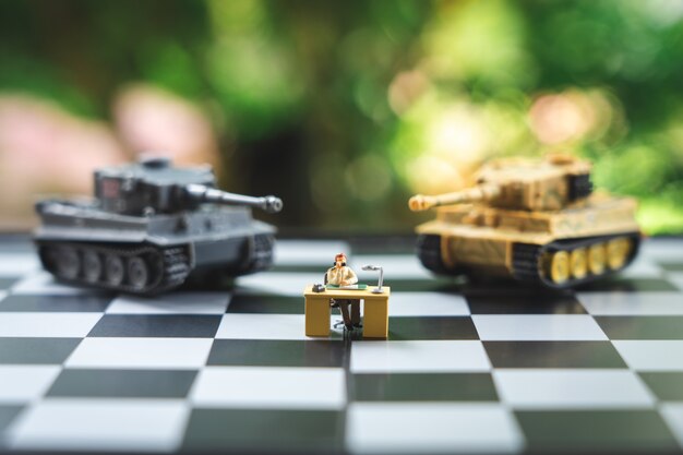 Empresários de pessoas em miniatura em pé em um tabuleiro de xadrez com um modelo de tanque