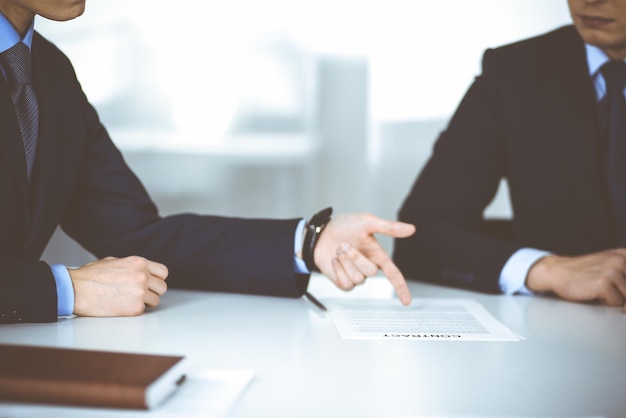 Los empresarios discuten un contrato, sentados en el escritorio de una oficina moderna. Empresario desconocido con un colega, abogados en negociación. Concepto de trabajo en equipo y asociación.