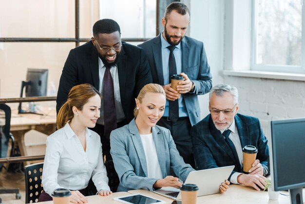 Empresários e mulheres de negócios multiculturais alegres olhando para um laptop