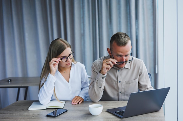 Empresários estão discutindo enquanto trabalham com laptop no escritório Empresários focados cooperando em um espaço de trabalho moderno Dois jovens empresários estão sentados juntos em uma mesa