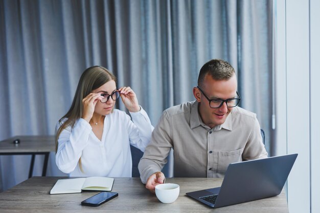 Empresários estão discutindo enquanto trabalham com laptop no escritório Empresários focados cooperando em um espaço de trabalho moderno Dois jovens empresários estão sentados juntos em uma mesa