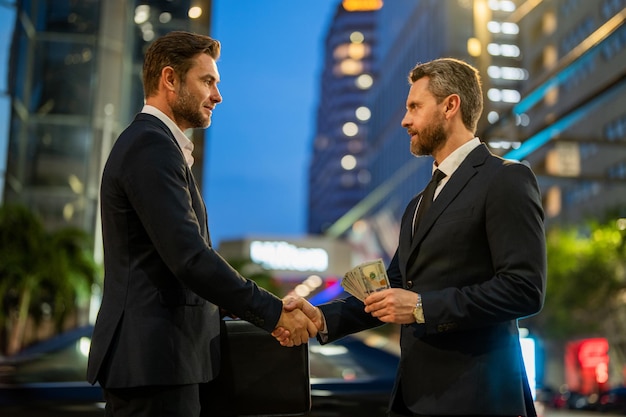 Empresarios estrechando la mano y recibiendo billetes empresario dando dinero al aire libre recibiendo dinero co