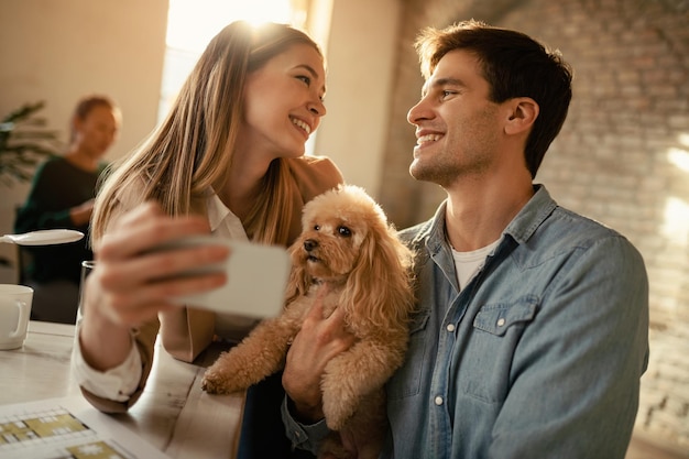 Empresarios felices que usan teléfonos inteligentes mientras se toman selfie con un caniche en la oficina