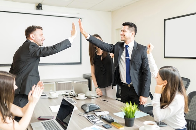 Empresários felizes dando mais cinco enquanto colegas do sexo feminino torcendo na mesa de conferência