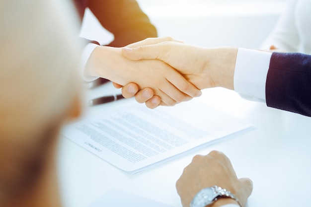 Empresários ou advogados apertando as mãos terminando reunião ou negociação no escritório ensolarado. Aperto de mão e parceria de negócios.