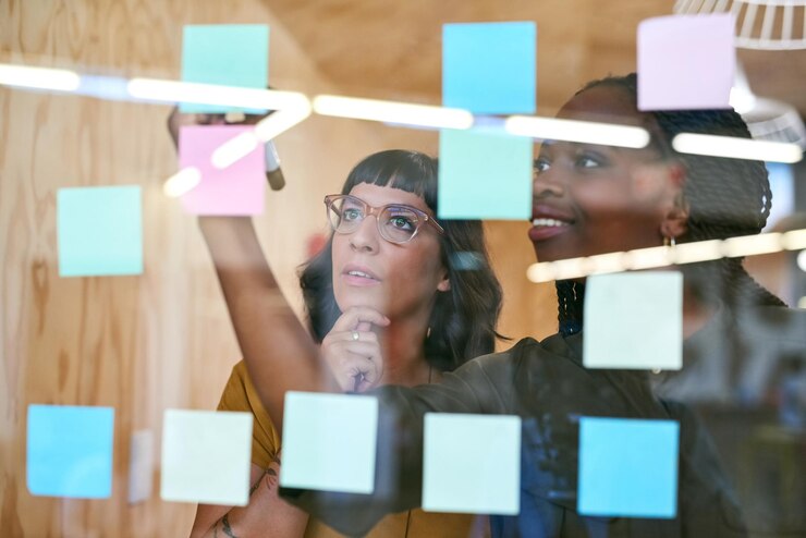 Foto empresários pensando e planejando com anotações em um escritório criativo para projeto de designer mulheres se unem para colaboração trabalho em equipe e ideias em uma parede de vidro com papel colorido e diversidade