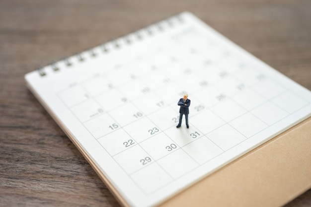 Empresarios de personas en miniatura de pie en el calendario blanco usando como concepto de negocio de fondo