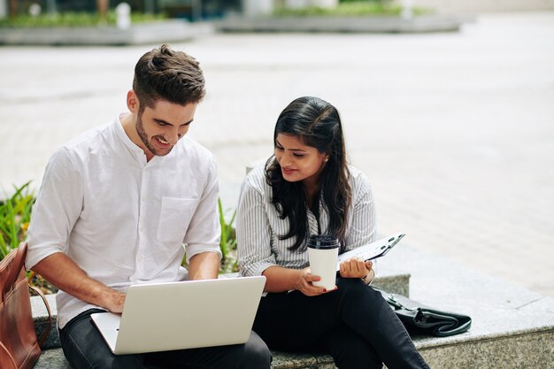 Empresários positivos discutindo informações na tela do laptop ao trabalhar ao ar livre