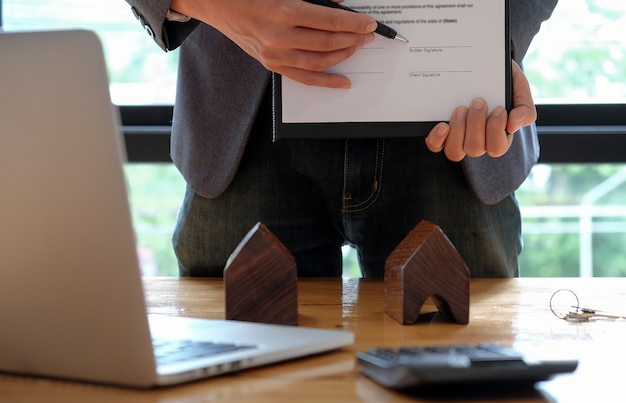 Foto empresários que vendem a casa apontando para a assinatura do contrato de venda no escritório.