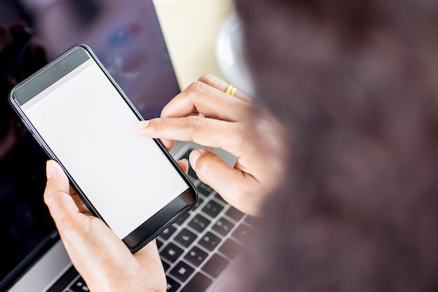 Los empresarios sentados en la oficina sobre el escritorio de trabajo con computadora y gráficos y café, sostienen teléfonos inteligentes con pantallas en blanco. Tomado desde el ángulo de visión superior