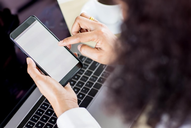 Los empresarios sentados en la oficina sobre el escritorio de trabajo con computadora y gráficos y café, sostienen teléfonos inteligentes con pantallas en blanco. Tomado desde el ángulo de visión superior