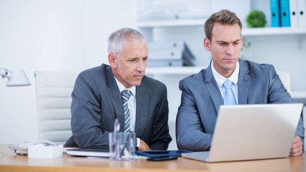 Empresarios serios trabajando juntos en la computadora portátil