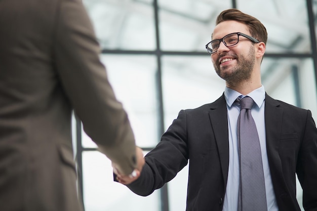 Empresarios sonrientes estrechando la mano comenzando una asociación de trabajo en equipo de pie en el pasillo del espacio de trabajo corporativo