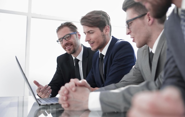 Empresarios sonrientes sentados en un escritorio frente a un concepto de negocio de computadora portátil