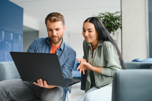 Los empresarios sonrientes trabajan colaborando en la lluvia de ideas de la computadora sobre el inicio de la empresa en la reunión de la oficina Diversos colegas motivados miran la pantalla de la computadora portátil y discuten ideas de proyectos de negocios juntos