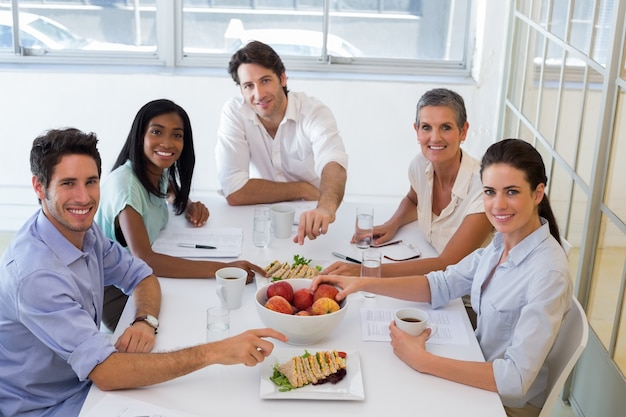 Empresários sorrindo na câmera comendo sanduiches e frutas para o almoço