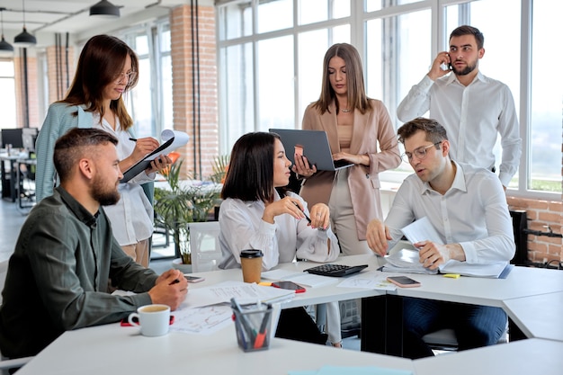 Empresários trabalhando em equipe em um escritório moderno, discutindo planos e estratégias de negócios, compartilham ideias. homens e mulheres caucasianos em trajes formais conversando, comunicando-se, sentados atrás da mesa