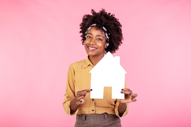 Empréstimo de seguro imóvel e conceito de família Alegre mulher afro-americana comprando ou vendendo casa segurando casa de papel e sorrindo otimista à procura de novo apartamento fundo branco