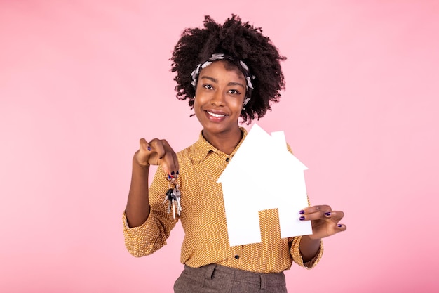 Empréstimo de seguro imóvel e conceito de família Surpreendida e espantada mulher negra segurando papel casa e chaves da casa procurando a casa perfeita fundo rosa