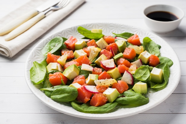 Empuje la ensalada hawaiana con los salmones, la espinaca del aguacate y las verduras en una placa en una tabla blanca.