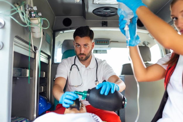 EMS-Paramediker-Team leistet verletztem Patienten auf dem Weg zum Gesundheitswesen medizinische Hilfe Krankenhaus Notfallpflege-Assistent verwendet eine Belüftungsmaske in einem Krankenwagen Junge Krankenschwester hält eine IV-Lösung