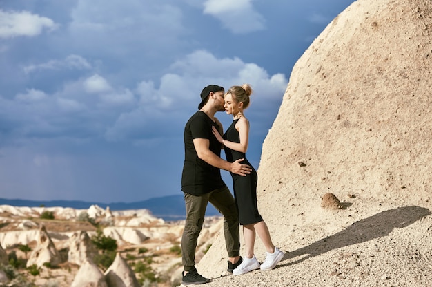 Enamorada Pareja oriental en montañas de Capadocia abrazos y besos. Amor y emociones amorosas pareja de vacaciones en Turquía. Closeup retrato hombre y mujer. Hermosos pendientes de luna creciente en orejas de niña