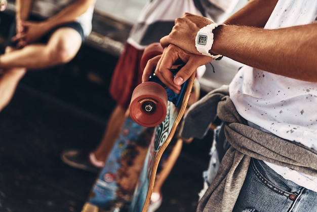 Enamorado de los deportes extremos. Primer plano de joven moderno apoyado en su patineta mientras pasa tiempo con amigos al aire libre