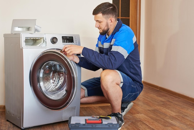 Encanador de macacão com ferramentas está consertando uma máquina de lavar em casa