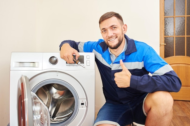 Encanador de macacão com ferramentas está consertando uma máquina de lavar em casa