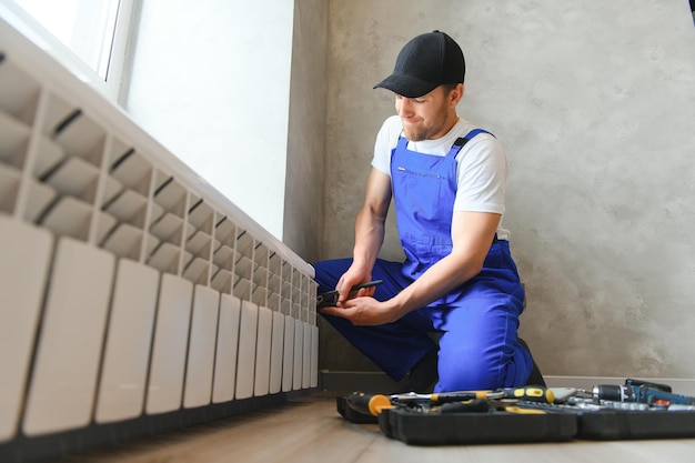 encanador jovem verificando o radiador ao instalar o sistema de aquecimento no apartamento