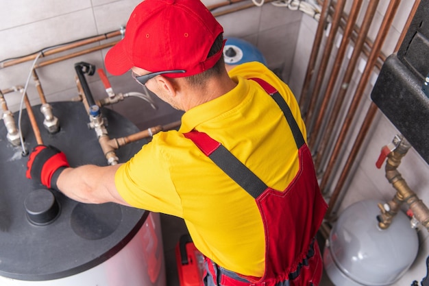 Foto encanador profissional caucasiano reparando aquecedor de água em tanque na sala de caldeiras de edifícios comerciais tema de manutenção de equipamentos de aquecimento