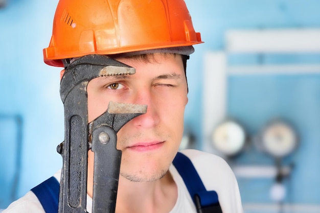 Encanador profissional em capacete olha diretamente para a câmera através de uma grande chave ajustável Grande retrato de um trabalhador real de 30 anos de idade