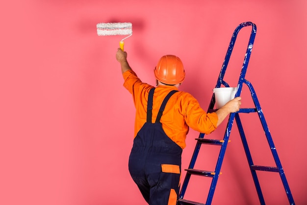 Le encanta su trabajo haciendo herramientas de reparación. Pintor que trabaja en el sitio de construcción. El hombre mayor usa rodillo en el trabajo de escalera en el apartamento. Artesano con rodillo de pintura.