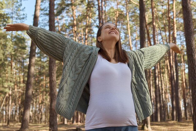 Foto encantada satisfecha mujer embarazada blanca descansando relajándose en un día soleado de primavera en el bosque madre embarazada con las manos extendidas respirando aire fresco disfrutando de los agradables momentos de su embarazo