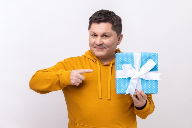 Encantado hombre de mediana edad con cabello oscuro sosteniendo una caja de regalo azul con una sonrisa señalando con el dedo