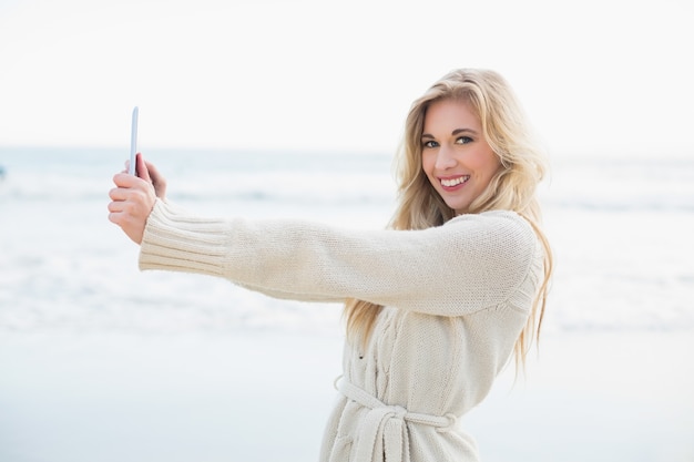 Encantado de mujer rubia en cardigan de lana tomando una foto de sí misma con una tablet pc