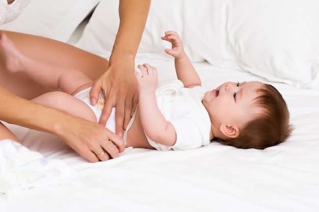 Encantador bebé mirando a su mamá y sonriendo mientras ella le cambia los pañales