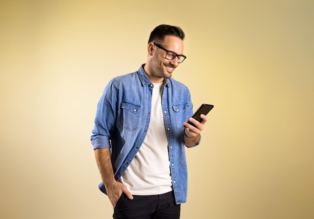 Encantador empresário masculino com a mão no bolso, sorrindo e enviando mensagens pelo celular