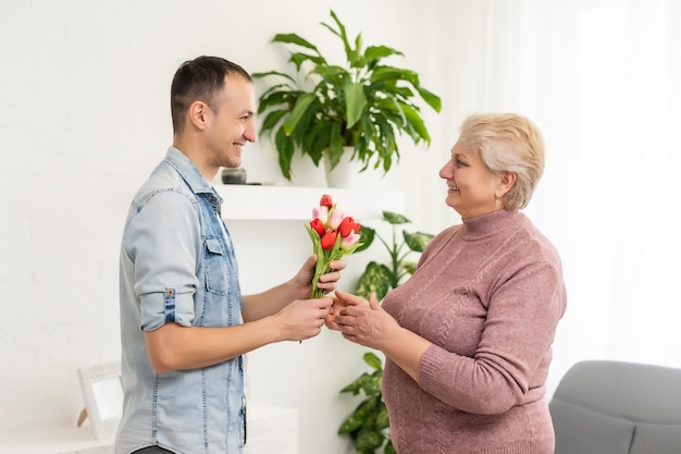 Encantador hijo volviendo a casa y llevando ramo de flores a su madre.