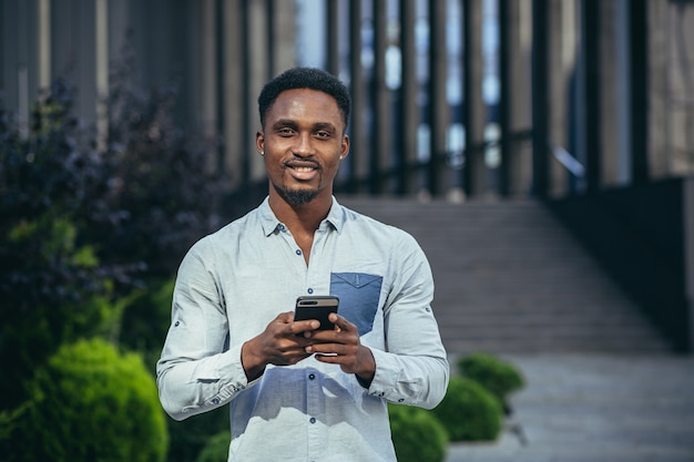 Encantador hombre afroamericano feliz mirando a cámara, sosteniendo el teléfono móvil en las manos sonriendo y feliz