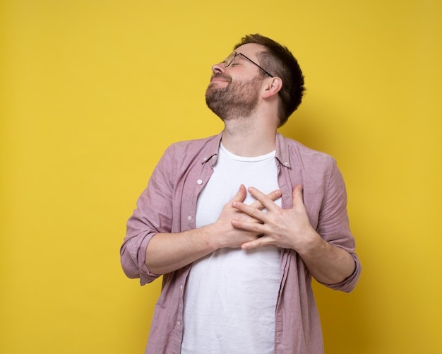 Encantador hombre romántico está enamorado, tiene las manos en el pecho en el área del corazón