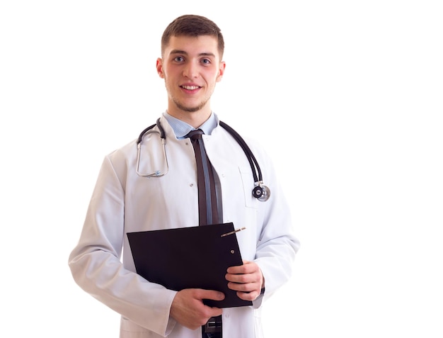 Encantador jovem com cabelo castanho em gravata de camisa azul e vestido de médico com estetoscópio