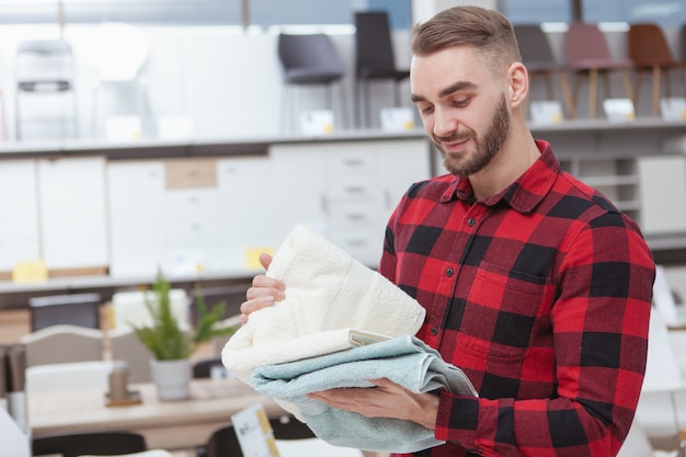 Encantador joven barbudo comprando ropa de casa en la tienda de muebles