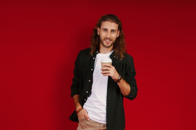 Encantador joven en ropa casual mirando a la cámara y sonriendo mientras está de pie contra la pared roja