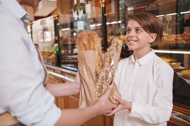 Encantador joven sonriendo con alegría, comprando pan fresco en la panadería