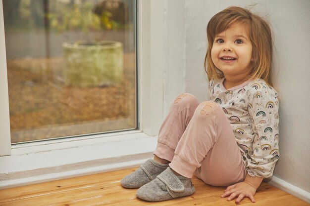 Encantador niño feliz con pantalones perforados sentado cerca de la ventana