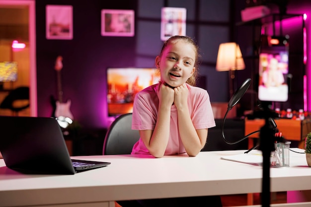 Un encantador niño pequeño grabando un video para una plataforma de redes sociales usando un teléfono inteligente Un joven influencer entreteniendo a sus seguidores creando contenido en un apartamento iluminado con neón rosa usando un teléfono en un trípode