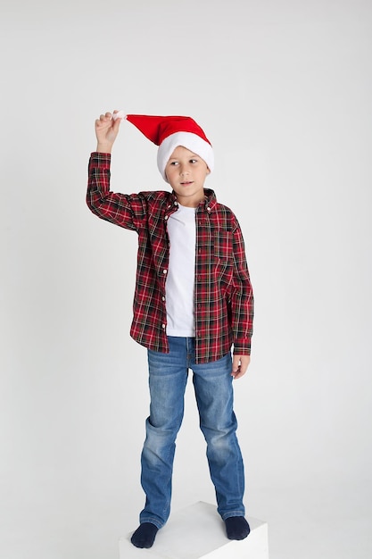 El encantador niño de siete años con gorra roja de Santa Claus sonríe habiendo estirado las manos hacia arriba La foto es ejecutada por aislados