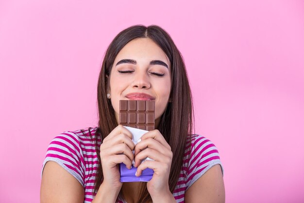 Una encantadora adolescente sonriente comiendo chocolate Imagen de una joven feliz y linda de pie aislada sobre un fondo rosa comiendo chocolate