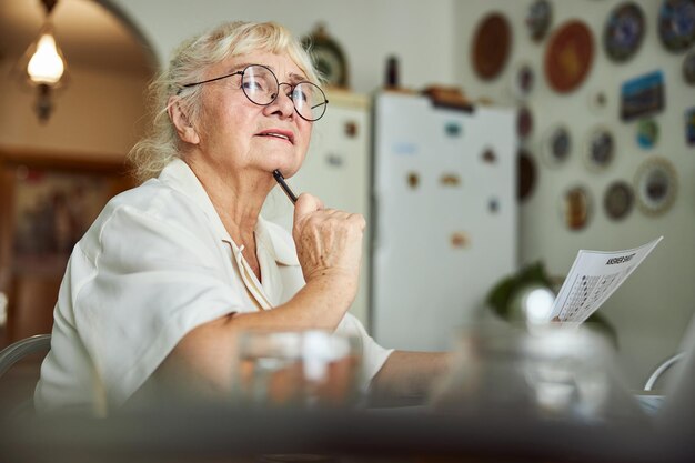 Encantadora anciana reflexionando sobre las respuestas para la prueba en casa